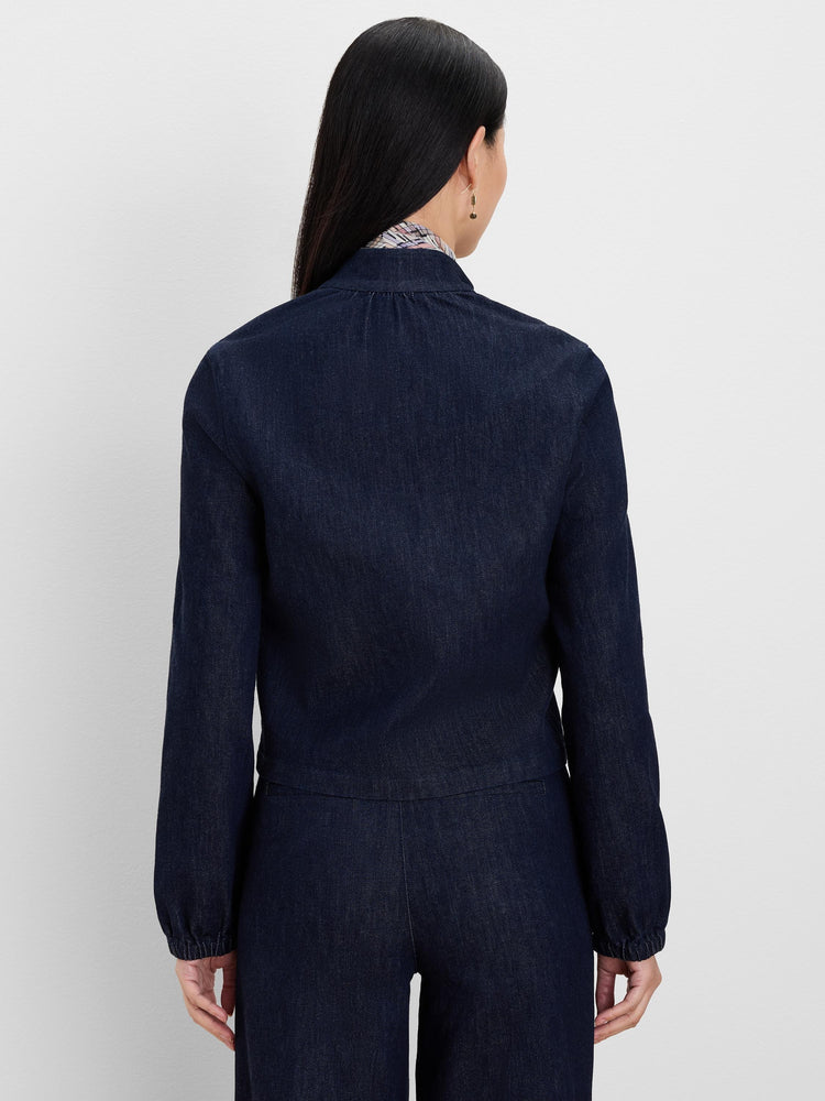 Dark indigo denim jacket, back view. Features a band collar and long sleeves with gathered elastic cuffs.