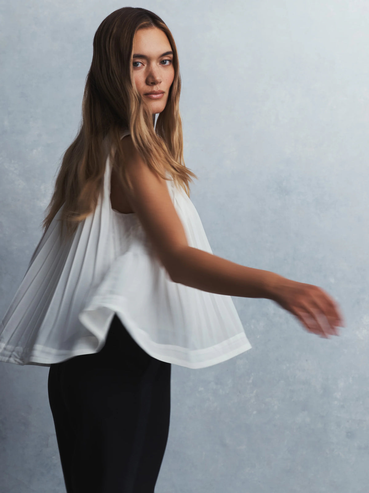 White sleeveless babydoll tank with a loose, flowing, pleated design.