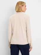 Loose beige long-sleeve shirt with buttoned cuffs, shown from the back over dark jeans.