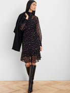 Black sheer dress with magenta and light yellow abstract dots, high neck, long sleeves, ruffled hem, above-knee length.