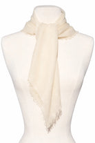 Cream scarf with frayed edges, tied on a mannequin.