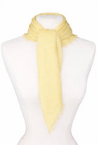 Pale yellow neck scarf tied on a mannequin with fringed edges.